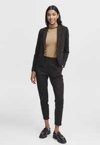 Black and white striped blazer and matching pants, paired with a tan turtleneck. Smooth fabric; single button closure; sleek, tapered fit.