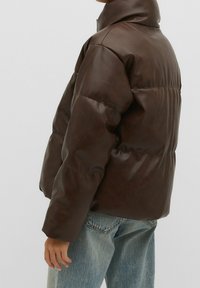 Bruine pufferjack gemaakt van faux leren, met een hoge kraag, doorgestikt ontwerp en een relaxte pasvorm, gecombineerd met lichtblauwe denim jeans.