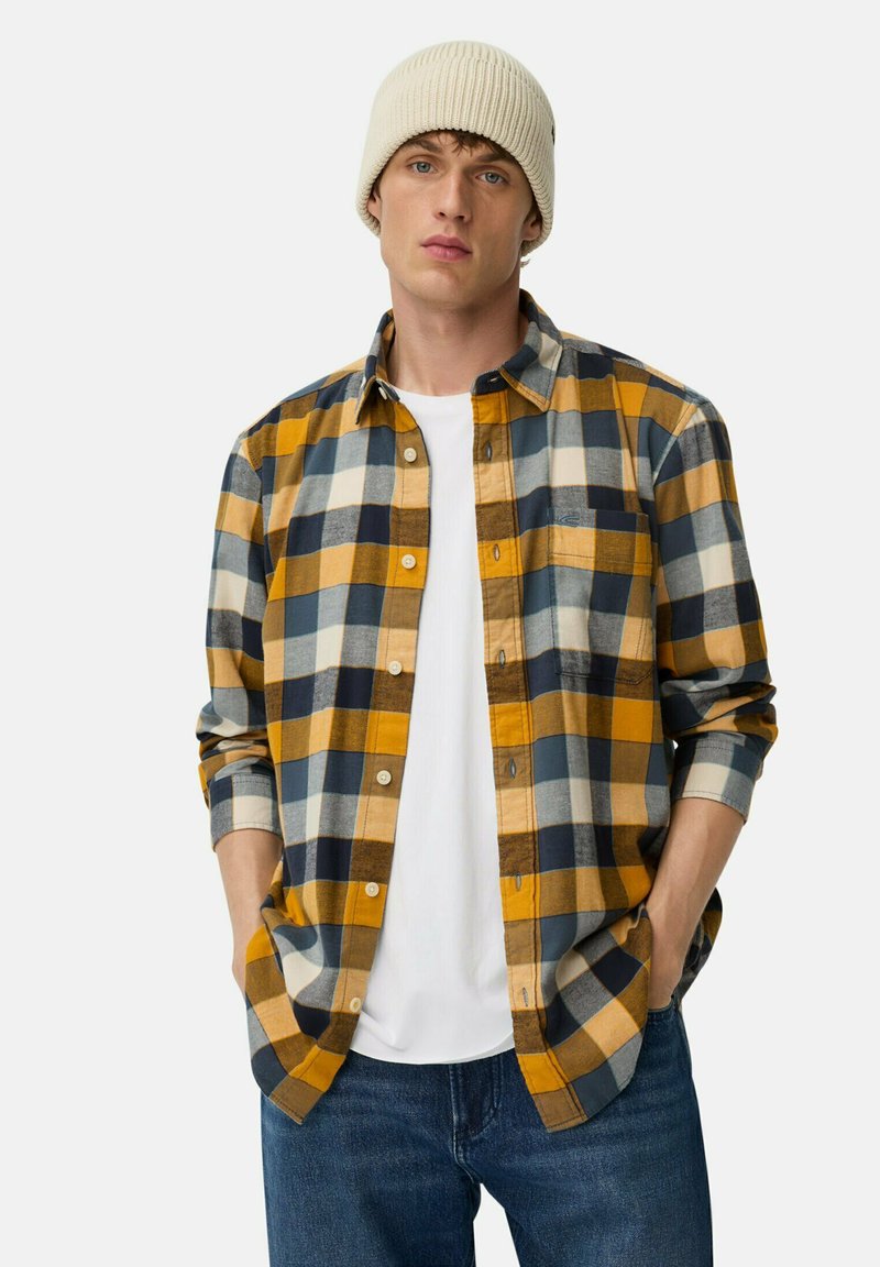 Geruit flanellen shirt in blauw, geel en crème met een knoopsluiting aan de voorkant, gecombineerd met een wit T-shirt en een blauwe spijkerbroek. Gebreide crème muts.