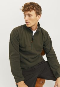 Dark green fleece pullover with half-zip and raised collar. Features raglan sleeves and patch pocket with orange zipper pull. Soft texture.