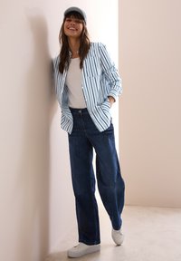Striped blue and white button-up shirt over a white t-shirt, paired with dark blue wide-leg jeans and white sneakers.