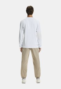 Biała koszula z długim rękawem i okrągłym dekoltem, w połączeniu z jasnobeżowymi spodniami. Prosty design, miękka faktura i minimalne detale brandingowe.