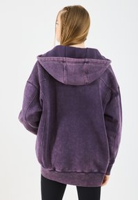 Felpa con cappuccio oversize in tessuto viola sfumato. Presenta un cappuccio ampio e polsini a coste. Texture morbida, design casual, senza loghi visibili.