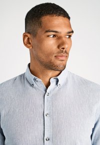 Jasnoniebieska koszula z długim rękawem o teksturowanym wykończeniu, z kołnierzykiem w szpic i srebrnymi guzikami. Posiada dopasowany krój oraz subtelny wzór.