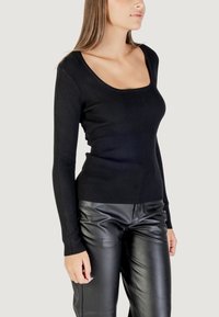 Maglione nero a maniche lunghe con scollo ampio, abbinato a pantaloni in pelle nera lucida. Tessuto morbido, design aderente.