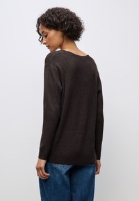 Brauner Strickpullover mit lockerem Schnitt und weiter Ausschnitt, kombiniert mit blauen Jeans, die eine dezente Textur und lange Ärmel aufweisen.