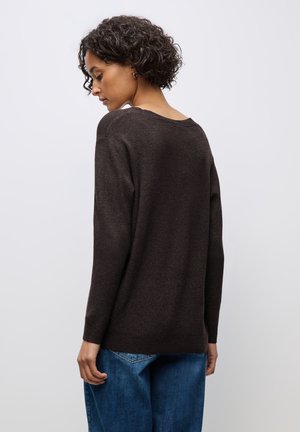 Maglione marrone lavorato a maglia con una vestibilità comoda e collo ampio, indossato con jeans blu in denim, che mostrano una fine texture e maniche lunghe.