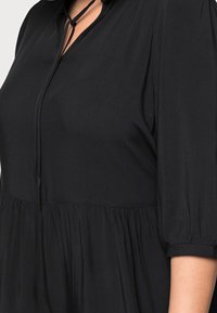 Blusa negra con un ajuste relajado, mangas globo de 3/4 y un dobladillo plisado. Fabricada en una suave tela lisa con un escote con abertura en forma de llave.