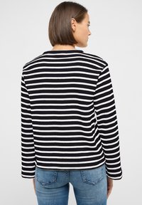 Mustvalge triibuline pikkade varrukatega särk, ümmarguse kaelusega ja kitsas lõikega, kombineeritud helesiniste teksadega. Nähtavad õmblused ja ääredetailid.