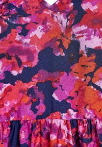 Tela con estampado floral en rojos, rosas y morados vibrantes sobre un fondo azul marino; presenta una superficie texturizada y un dobladillo con volantes.