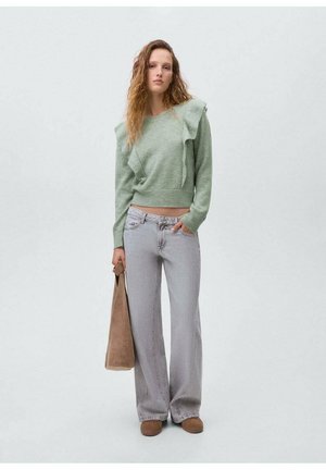 Maglione verde chiaro con dettagli arricciati, abbinato a jeans larghi grigi chiari e scarpe slip-on marroni. Modella con una borsa marrone.