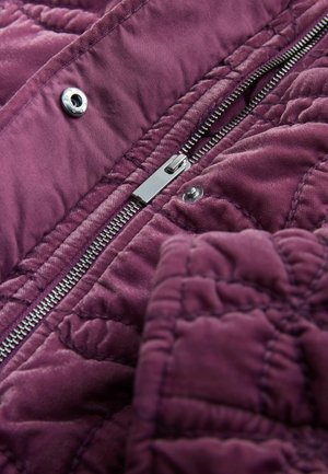 Lila steppelt szövet sima textúrával, ezüst cipzárral és patentzárral, amely kiemeli a részletes varrást.