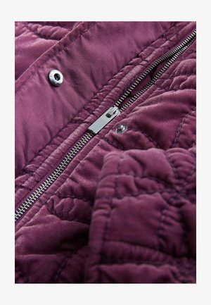 Lilla tikitud kangas, millel on sile tekstuur, hõbedase luku ja trukiga sulgur, rõhutades selle detailset õmblust.