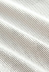 Gros plan sur un tissu blanc texturé avec de fines côtes verticales et de doux plis créant des ombres douces.