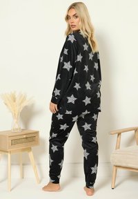 Svart velour-pyjamasset med vita stjärnmönster. T-shirt med långa ärmar och figurnära byxor, med en mjuk textur och avslappnad passform.