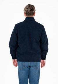 Giacca in corduroy blu navy con colletto classico, maniche lunghe e schiena dritta, abbinata a jeans in denim blu.