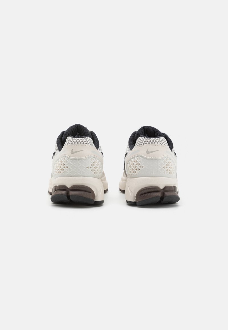 Baskets Nike avec une tige en mesh blanche et noire, accents texturés triangulaires, col rembourré et semelle en caoutchouc avec un design bicolore.