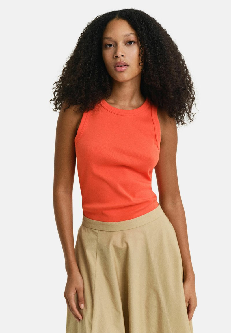 Oranges ärmelloses Tanktop aus geripptem Stoff, taillierter Schnitt, kombiniert mit einem fließenden beigen Rock mit breitem Bund und A-Linien-Form.