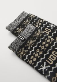 Black and gray knitted socks feature a Fair Isle pattern with cream accents. A branded black label is visible on the side.