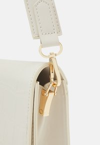 Borsa bianca in ecopelle con finitura testurizzata, ferrature dorate e tracolla con chiusura a clip. Dettagli notevoli includono cuciture e un design elegante.