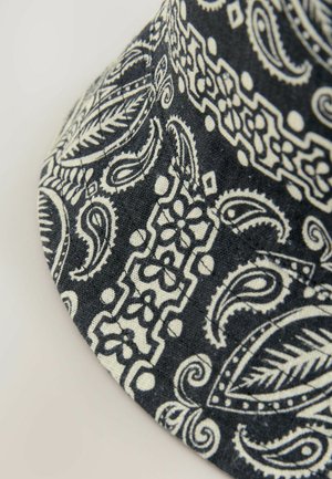 Crno-bijeli šešir s uzorkom, koji ima paisley i cvjetne motive, izrađen je od tkanine s teksturiranim završetkom i vidljivim šavovima.