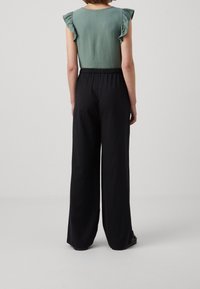 Grön texturerad topp med volangärmar, kombinerad med svarta vida byxor. Outfiten har en avslappnad passform och elastisk midja.