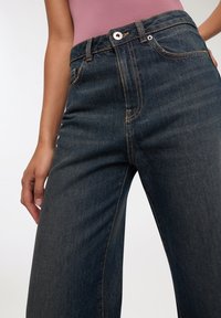 Jeans in denim blu scuro con vita alta, caratterizzati da cuciture prominenti e chiusura con bottone. Tessuto liscio con design a gamba dritta.