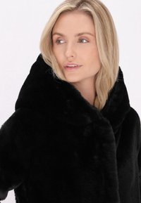 Cappotto in pelliccia sintetica nera con un ampio colletto morbido, caratterizzato da una texture liscia e una vestibilità comoda, progettato per offrire calore e comfort.