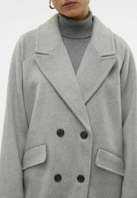 Cappotto doppiopetto in misto lana grigio con due tasche frontali e grandi bottoni neri. Presenta un ampio colletto a punta e una texture morbida.