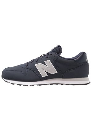 Granatowy sneaker New Balance z białą podeszwą, szarym logo "N" i czarnymi sznurowadłami, pokazany z boku na białym tle.