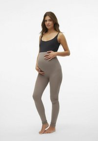 Legginsy ciążowe w miękkim beżowym kolorze, zestawione z ciemnym topem bez rękawów. Legginsy mają gładką fakturę i wysoki stan.