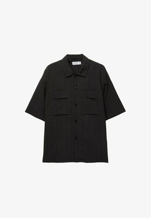 Chemise à manches courtes, boutonnée, en tissu noir texturé avec deux poches poitrine et un col classique. Les boutons sont noirs.