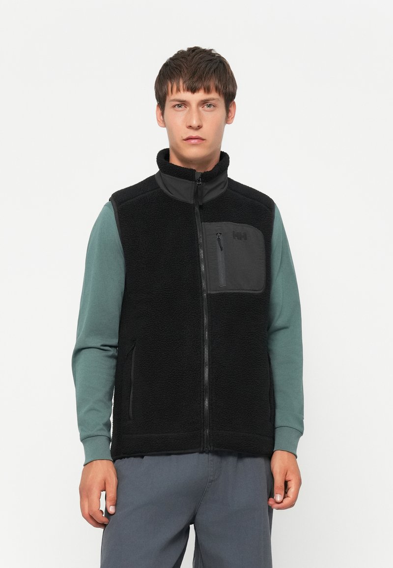 Zwarte fleece vest met ritssluiting aan de voorkant, opstaande kraag en een borstzak. Kenmerkt zich door een gestructureerd materiaal en wordt gedragen over een teal langslavenshirt.
