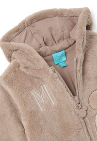 Chaqueta de forro polar beige con capucha, que presenta un "M" bordado, un zipper con un tirador en forma de Mickey Mouse y un forro interior suave.