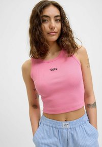 Roza rebrasta majica s kratkimi rokavi in krožnim izrezom ter majhnim črnim logotipom, kombinirana s svetlo modrimi hlačami s črtami in elastičnim pasom.