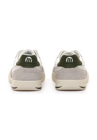 Sneakers bianche e grigie con texture in suede, caratterizzate da accentuazioni verdi sul tallone e un logo circolare. Il design include colletto imbottito e suola a contrasto.