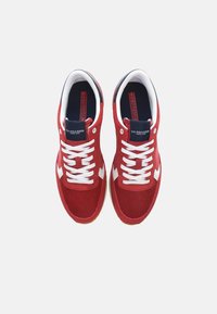 Röda sportiga sneakers med vita accenter och snören. Har ett meshtyg på ovansidan och en gummisula, med en varumärkeslogotyp på tungan.