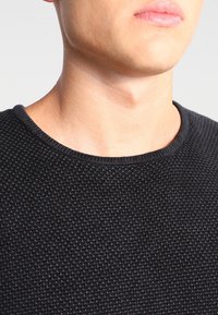 Maglione nero a maglia con un motivo testurizzato e un collo rotondo semplice. Il tessuto appare morbido e leggermente elastico.
