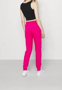 Pantaloni della tuta rosa con cintura elastica e polsini; presenta una tasca laterale. Abbinati a un top corto nero e sneakers bianche.