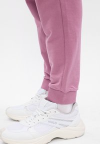 Rózsaszín pamut sportnadrág, bordás mandzsettákkal, fehér sneakers-szel, amelyek hálós panelek és "HUGO" márkajelzés található az oldalán.