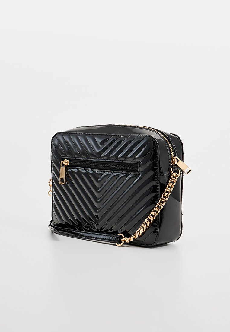 Sac bandoulière en cuir verni noir avec un motif chevron, bandoulière en chaîne dorée et poche zippée à l'avant. Compartiment principal zippé.