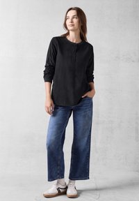 Maglietta nera a maniche lunghe con una patta di bottoni, abbinata a jeans in denim azzurro chiaro larghi e sneakers bianche con accenti neri.