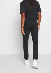 Černé bavlněné tričko a odpovídající tepláky s elastickým pasem, zúženými nohavicemi a žebrovanými manžetami, doplněné bílými teniskami.