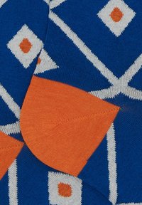 Tessuto a maglia con uno sfondo blu presenta motivi a diamante bianchi e arancioni. La trama è liscia con una sezione accentuata arancione visibile.