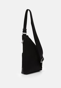 Borsa a tracolla nera a forma triangolare, realizzata in stoffa con una texture liscia, dotata di una tracolla regolabile e dettagli in metallo argentato.