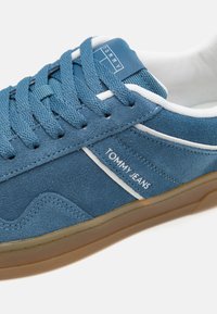 Plave suede tenisice s bijelim naglascima i vezicama. Imaju logo na bočnoj strani i teksturiranu gumenu đonu. Dizajn s okruglim vrhom.