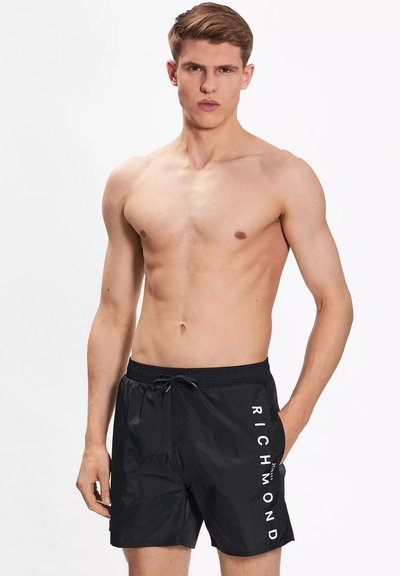 Pantaloni da nuoto neri realizzati in materiale leggero. Presentano una vita elasticizzata con cordino e il logo "RICHMOND" stampato in bianco lungo il lato.