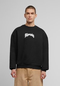 Zwarte sweatshirt met een ronde hals en oversized pasvorm. Bevat gestileerde witte tekst op de borst. Zacht materiaal, casual ontwerp.