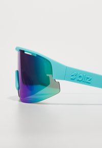 Aqua blue sunglasses with gradient purple-green lenses, sleek wraparound design, and textured logo on the temple. Lightweight frame.