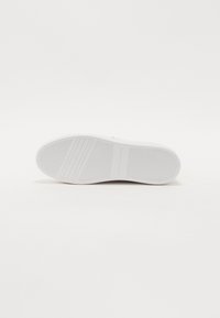 Semelle de basket blanche avec un motif antidérapant texturé et un logo en relief. Forme plate avec un bout arrondi et une finition lisse.